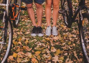 homme en converse noires et femme en converse blanches avec vélos feuilles automne